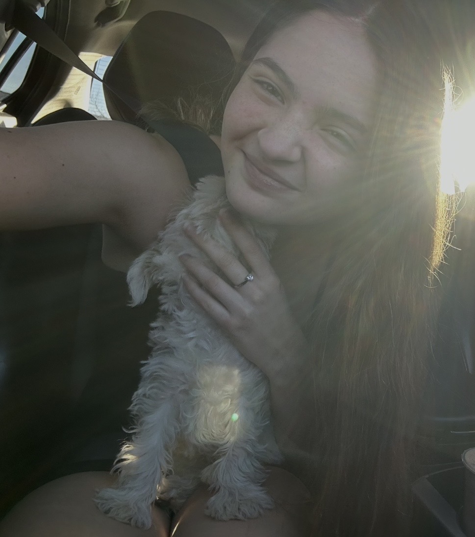 A sitter smiling with a small white puppy in warm sunset light